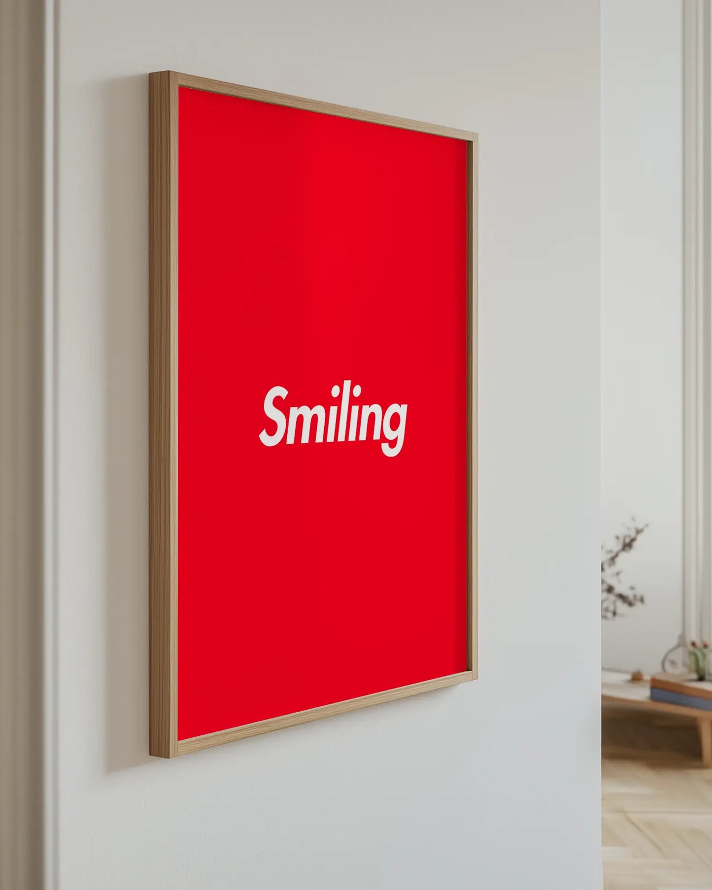 Red poster with 'Smiling' text in a wooden frame on a white wall.