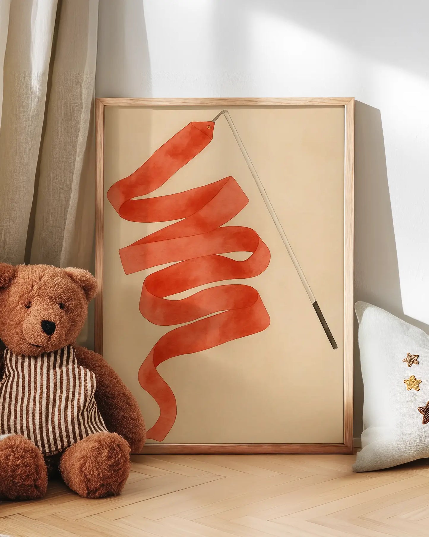 Artwork with a red ribbon on a wall next to a teddy bear and decorative pillow.
