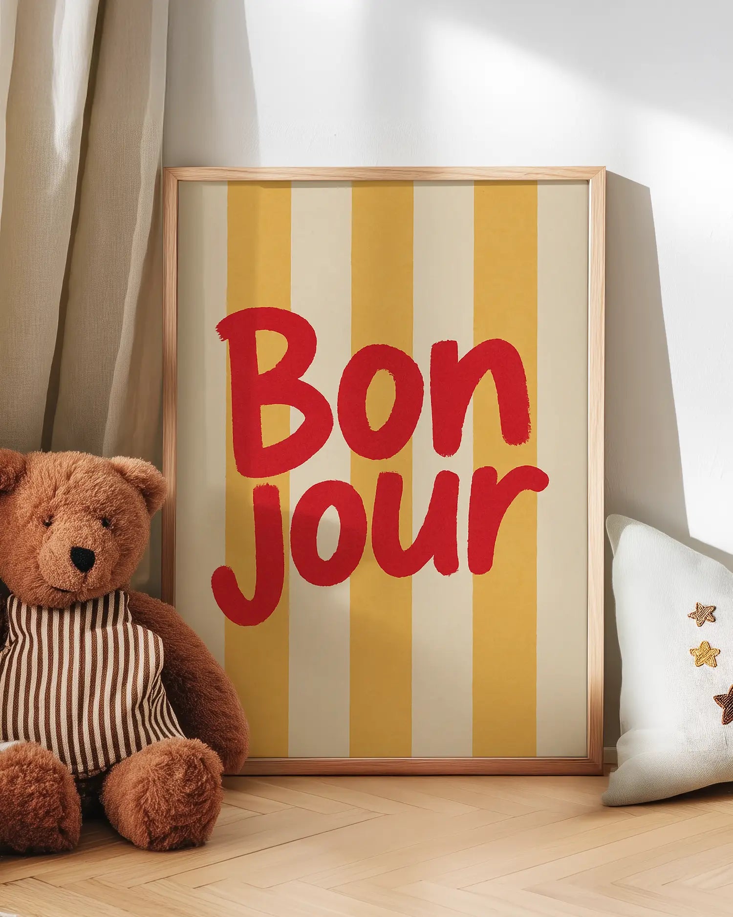 Framed 'Bonjour' sign with a teddy bear and decorative pillow on a wooden floor.