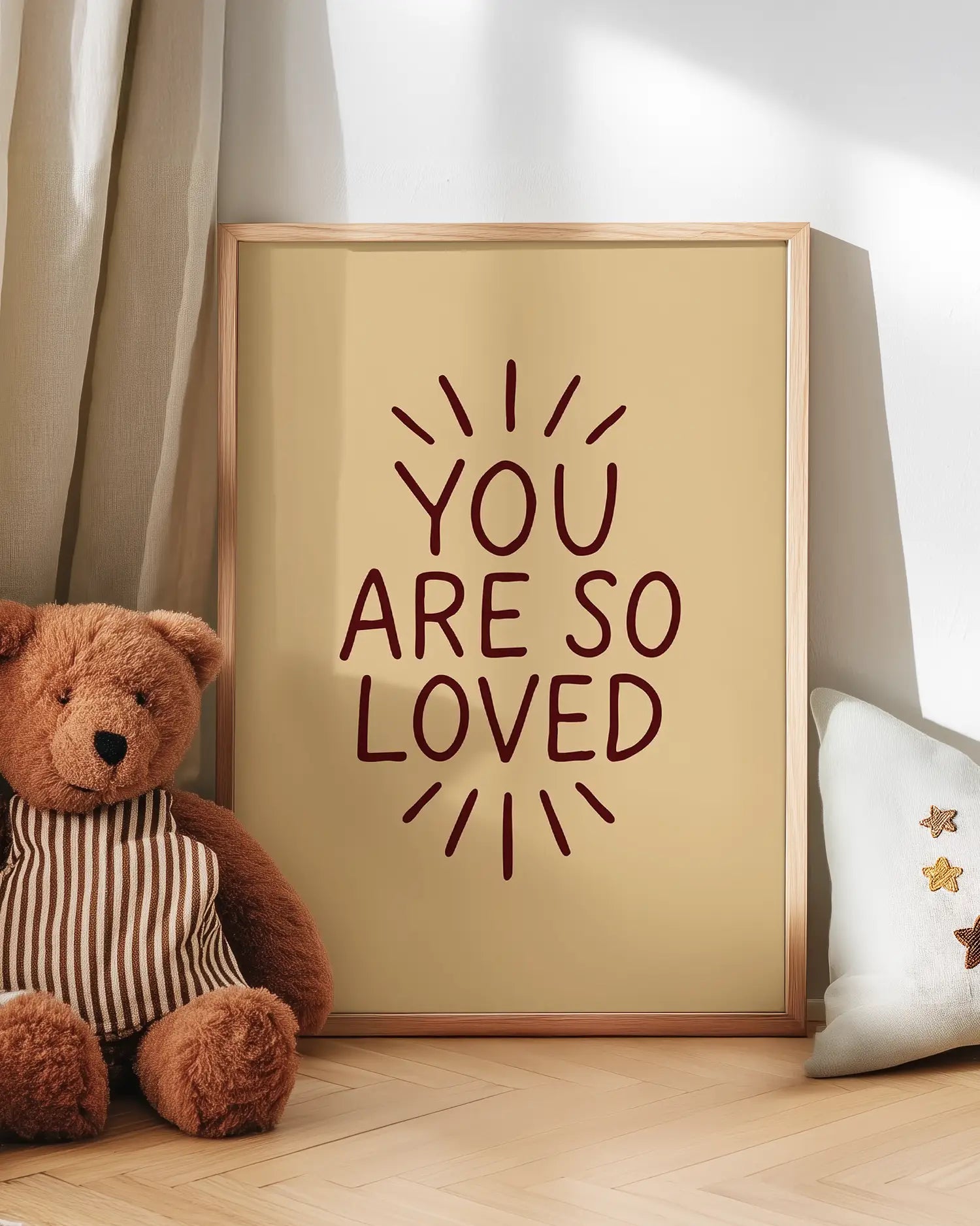 Framed artwork with 'You are so loved' text next to a teddy bear on a wooden floor.