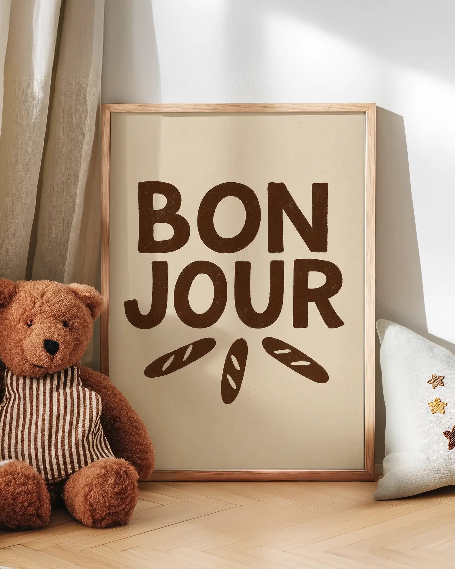 'Bonjour' poster with a teddy bear and decorative pillow on a wooden floor.